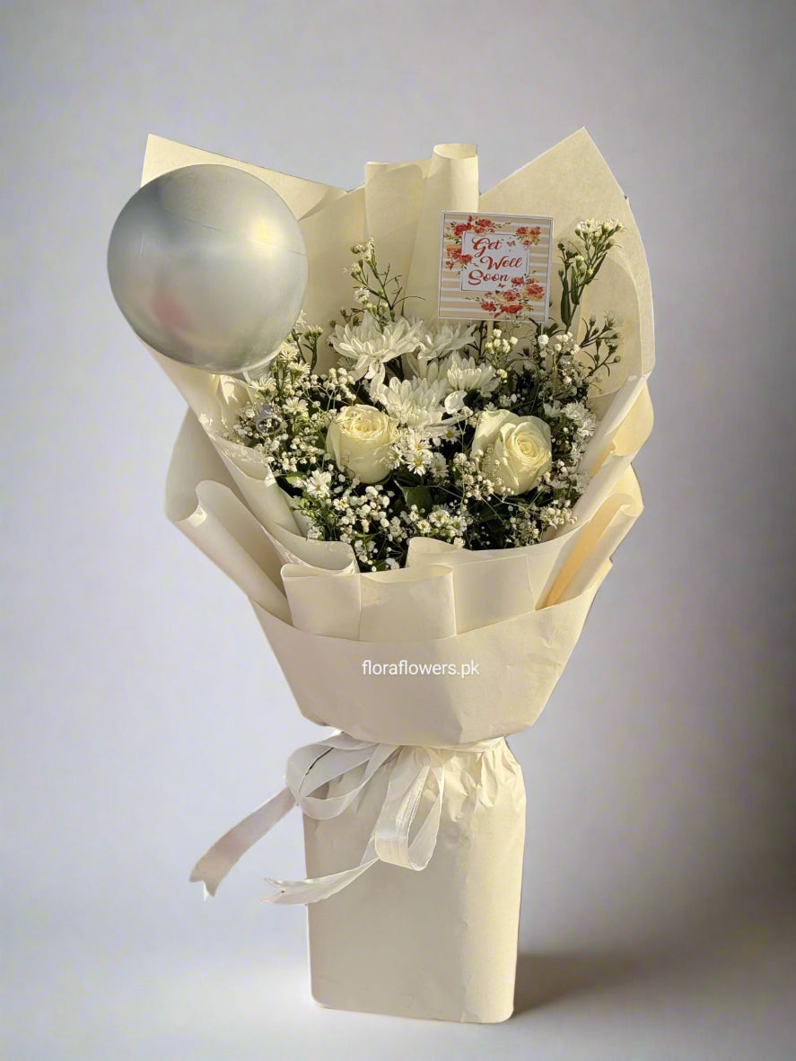 A bouquet of flowers consisting of white roses and baby's breath, wrapped in white paper with a decorative ribbon and a round silver ornament on top.