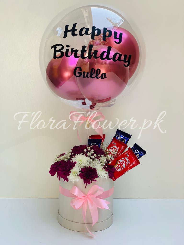 A gift arrangement featuring a balloon with 'Happy Birthday' text, an assortment of chocolates, and a bouquet of white and purple chrysanthemums.