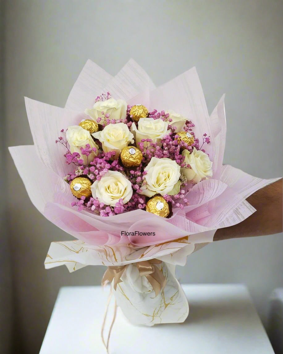 A bouquet of white roses mixed with baby's breath and Ferrero Rocher candies, wrapped in pink and white paper.