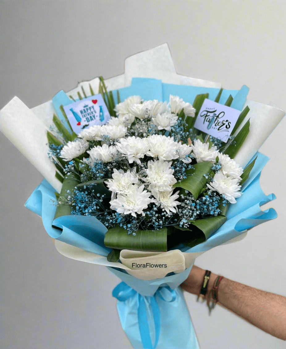 A bouquet of white and blue flowers with baby's breath, wrapped in blue and white premium wrapping paper with the brand name 'FloraFlowers' visible.