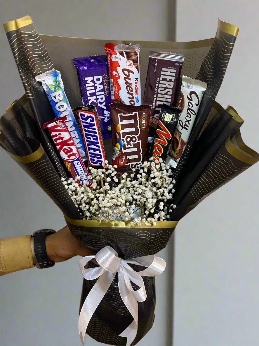 A bouquet of chocolate bars arranged in a V-shape with baby's breath flowers, wrapped with black paper and tied with a white ribbon.
