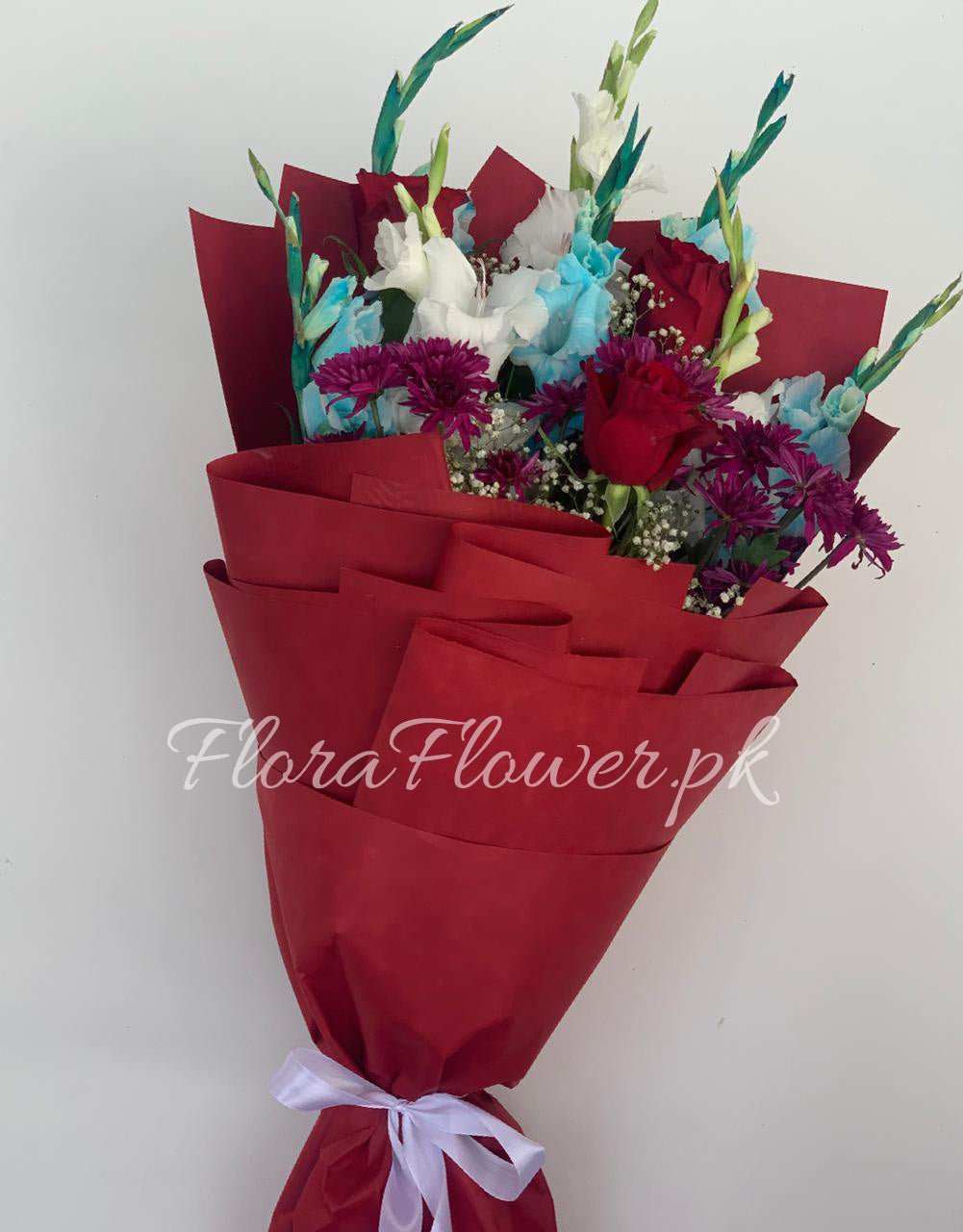 A bouquet of roses, chrysanthemums, and baby's breath wrapped in red and available wrapping sheets with a white ribbon.