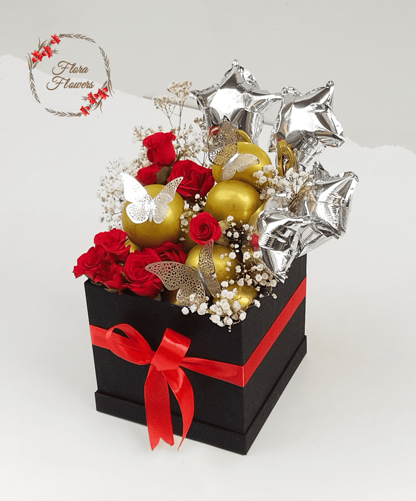 A gift basket containing an assortment of items including red roses, golden balloons, silver star-shaped balloons, and decorative butterflies.
