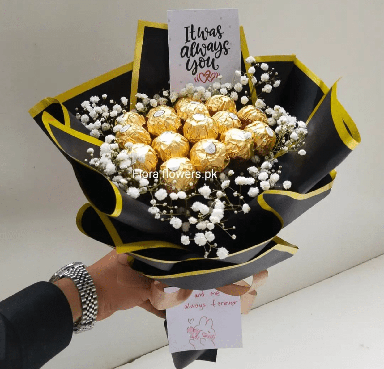 Bouquet of gold Ferrero Rocher chocolates with white flowers and a card in black and yellow packaging.