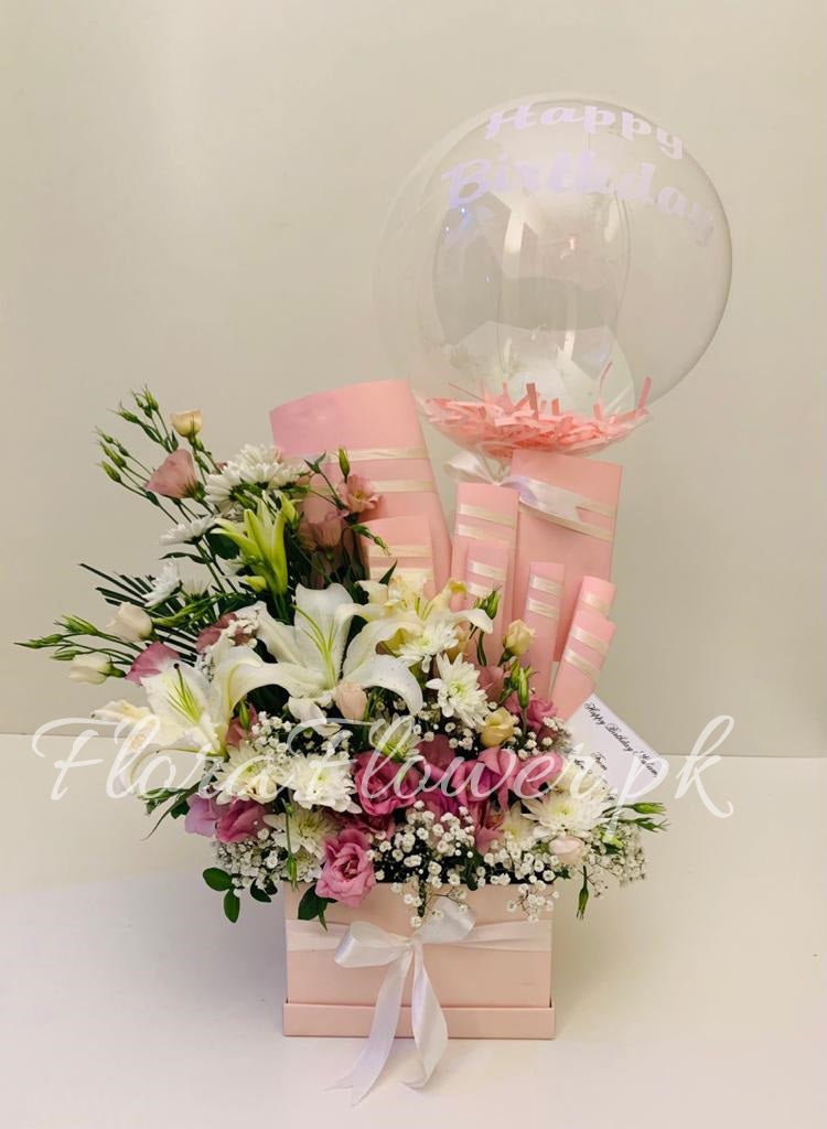 A gift arrangement featuring a box of flowers with Chrysanthemums, Baby's Breath, and a Lily, accompanied by chocolates including Snickers, Mars, Dairy Milk, and a Kitkat, and a balloon with customizable text.