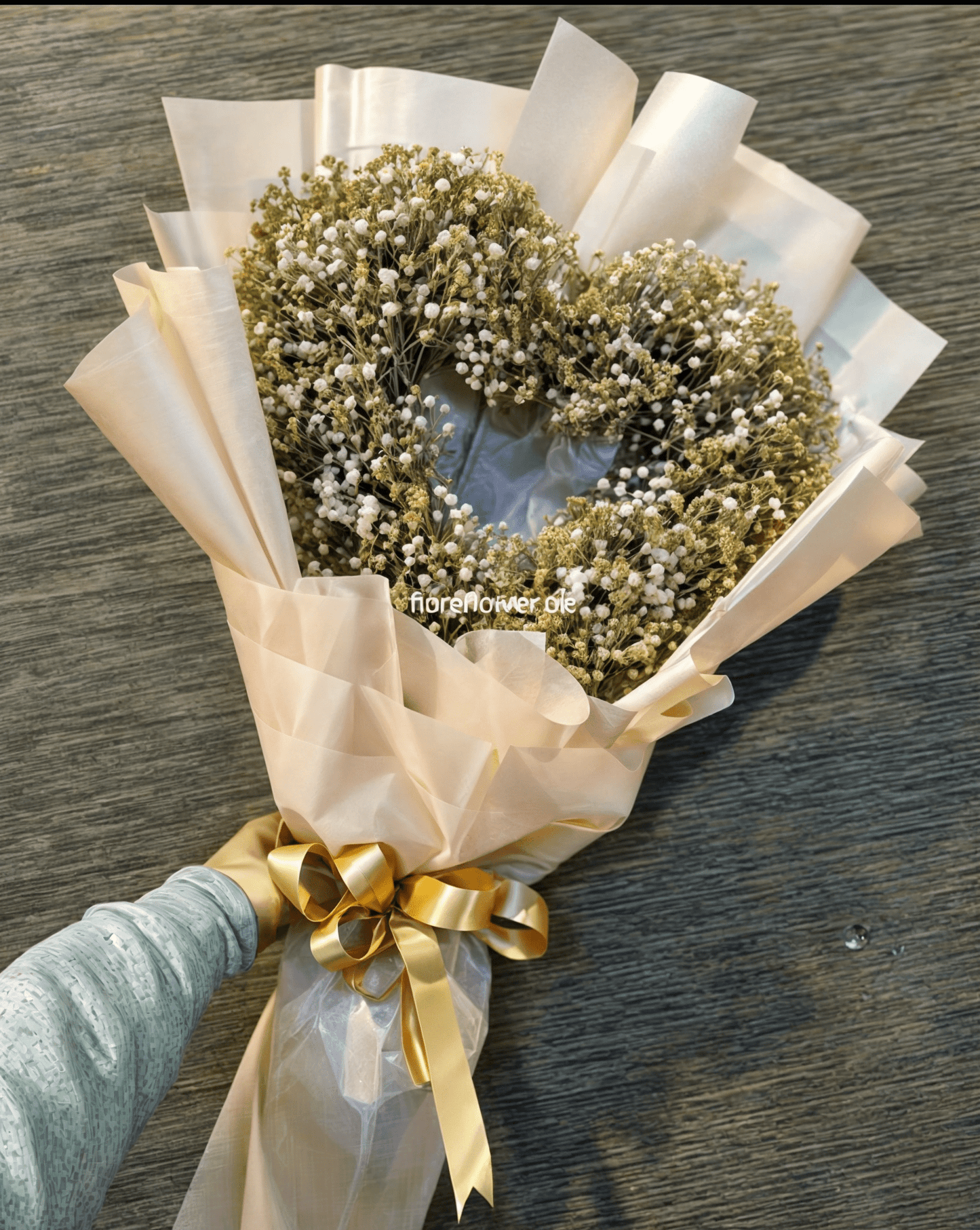 Bouquet of baby's breath flowers wrapped in white paper with a gold ribbon on a wooden surface.