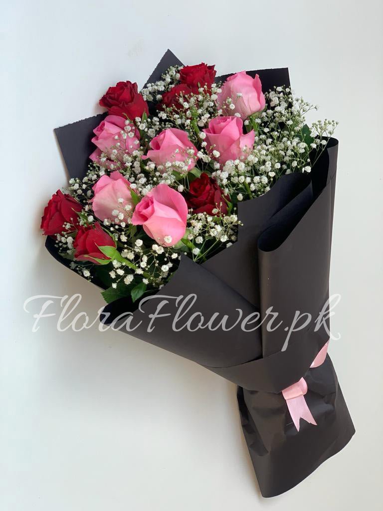 A bouquet of flowers consisting of pink and red roses with baby's breath, wrapped in black paper with a pink ribbon.