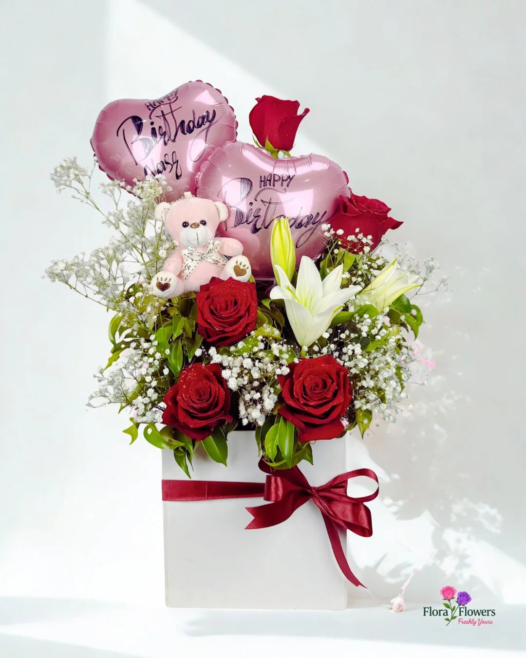 Bouquet of red roses, white lilies, and a teddy bear with birthday balloons on a white background.. Send flowers to lahore. send flowers to Pakistan
