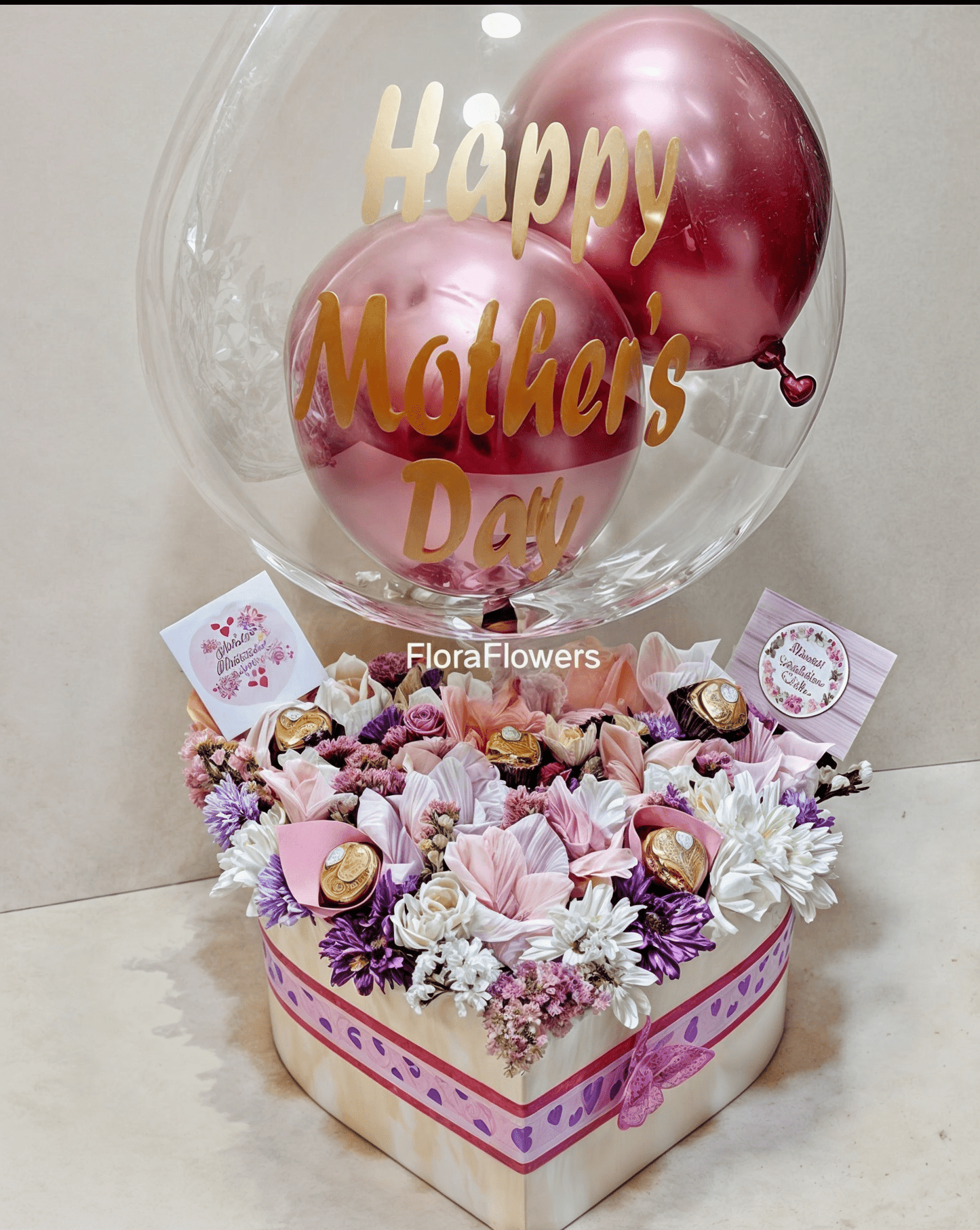 Heart-shaped box of flowers with 'Happy Mother's Day' balloons and FloraFlowers branding.