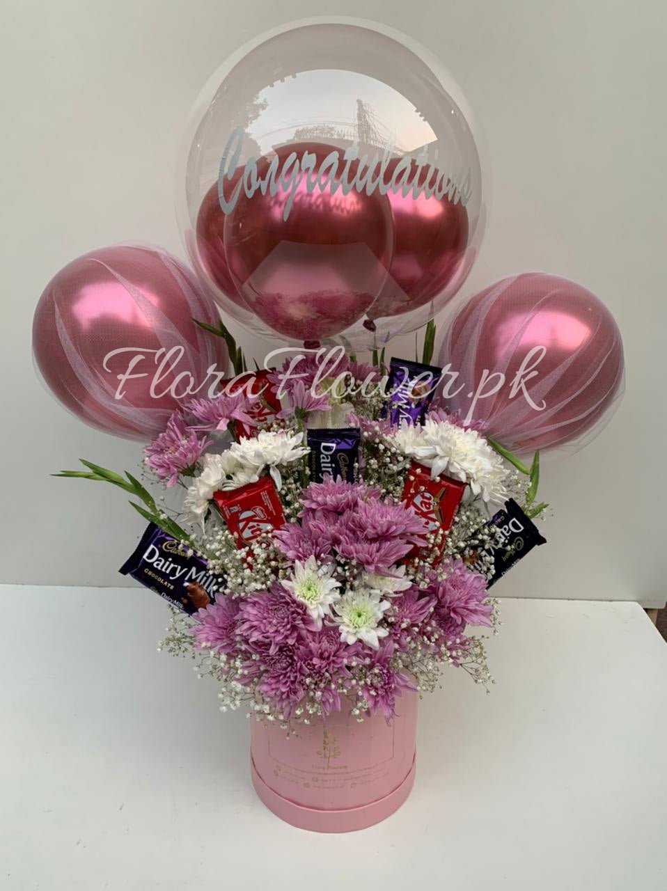 Floral arrangement with pink balloons and Cadbury Dairy Milk chocolate bars on a white background
