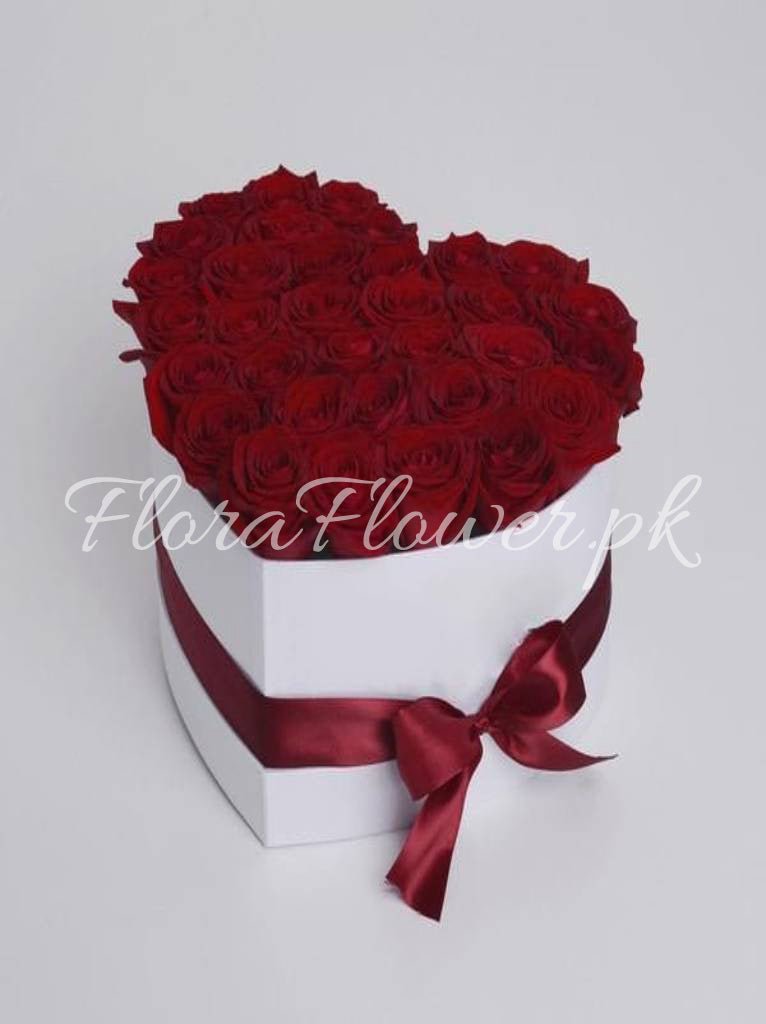 A heart-shaped arrangement of red roses presented in a white box with a red ribbon.