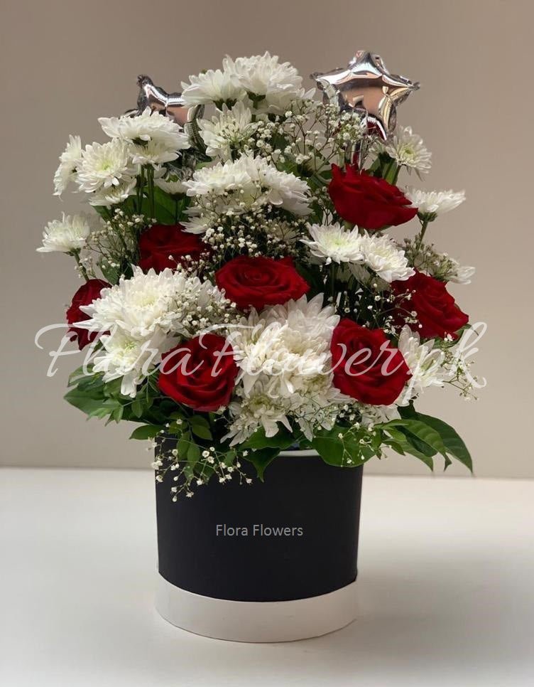 A flower arrangement containing red roses, white chrysanthemums, and baby's breath presented in a round container, with decorative stars on top.