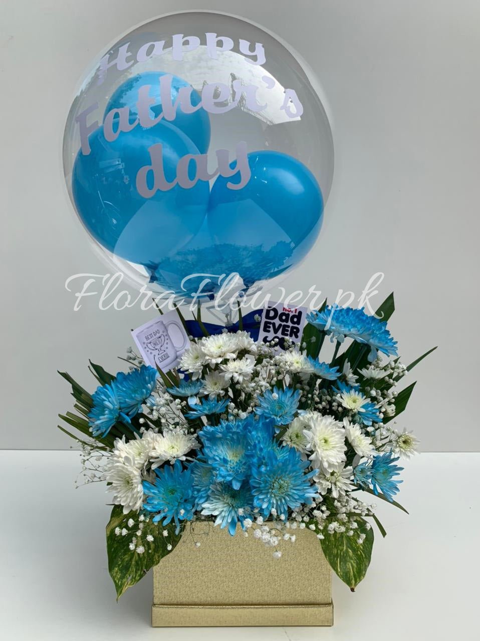 A floral arrangement with blue and white flowers, accompanied by a blue balloon with text 'Happy Father's Day', presented in a box.