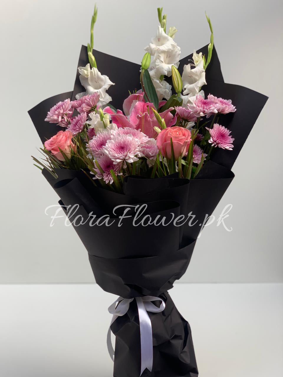 A bouquet of flowers including roses, chrysanthemums, a lily, and baby's breath, wrapped in black paper with a silver ribbon.