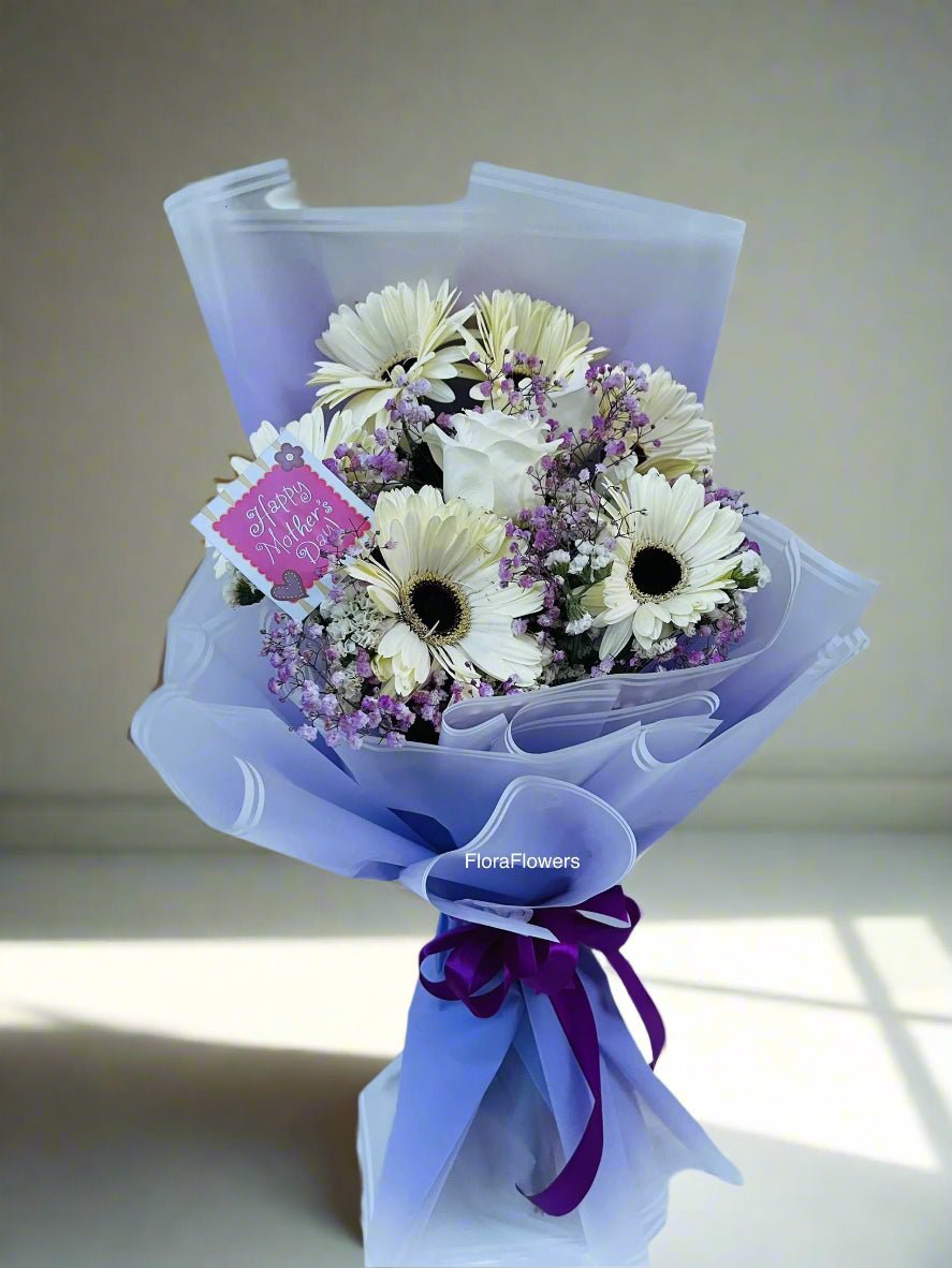 A bouquet of white gerbera daisies, baby's breath, and a rose, wrapped in premium wrapping sheets with a purple ribbon.
