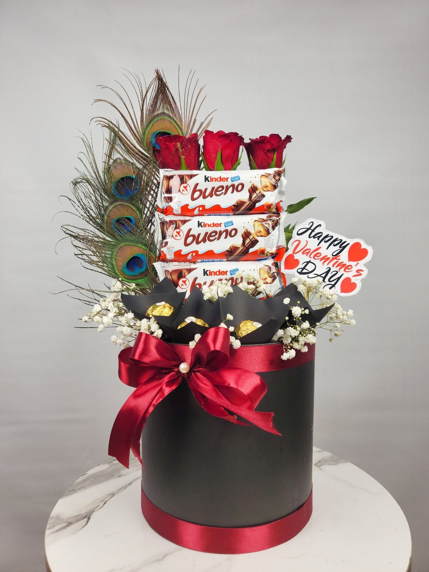 Valentine's Day gift basket with flowers, chocolates, and a peacock feather on a gray background. Send flowers to islamabad. send flowers to pakistan