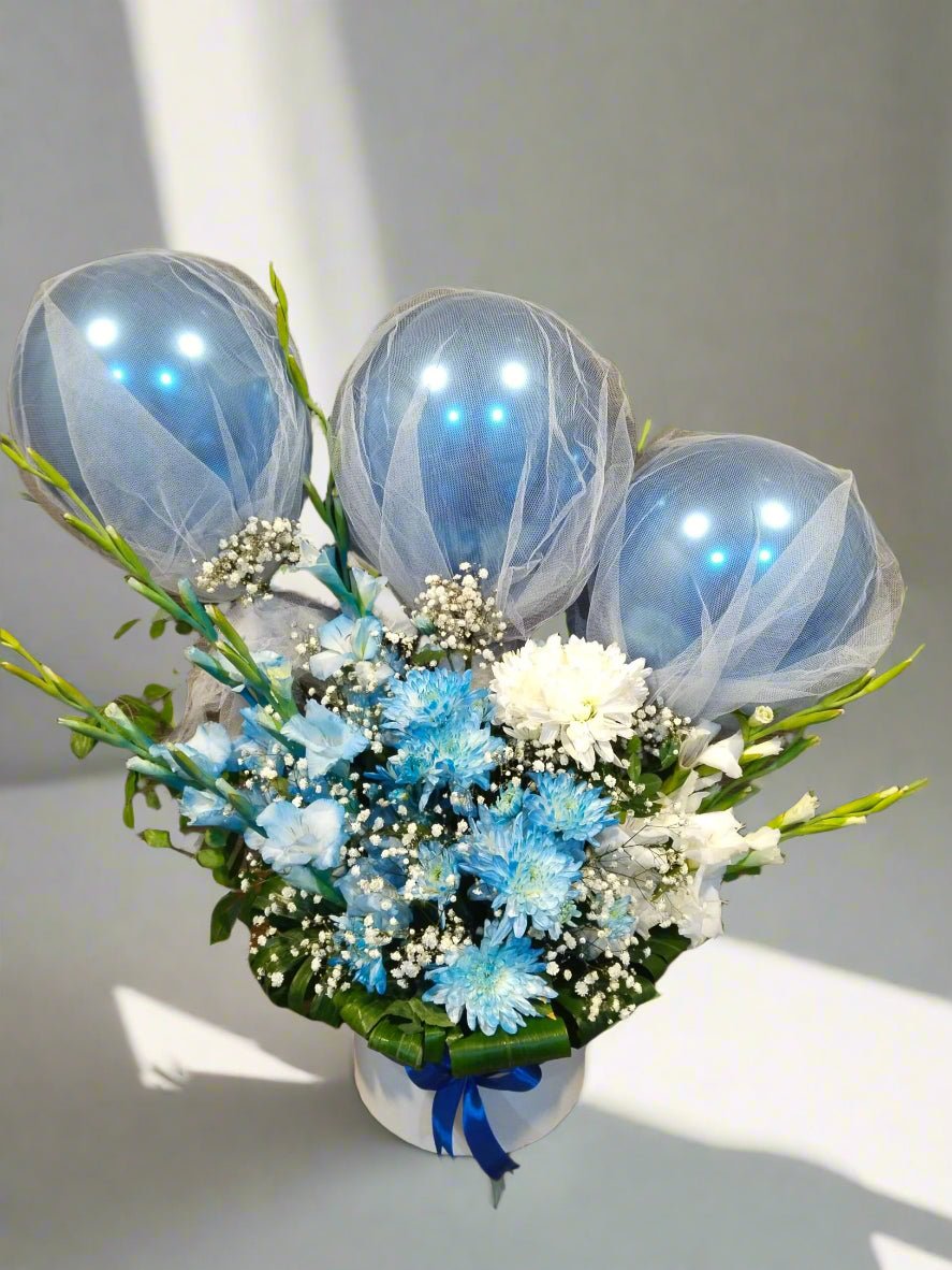 A bouquet of flowers with blue balloons incorporated into the arrangement, displayed on a table.