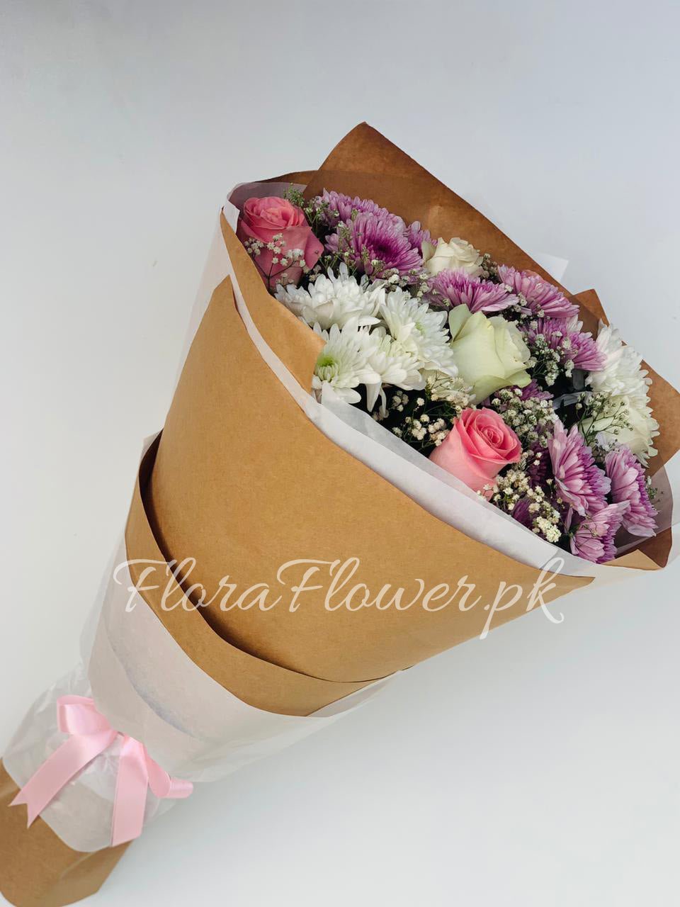 A bouquet of roses, chrysanthemums, and baby's breath flowers wrapped in brown paper with a pink ribbon.