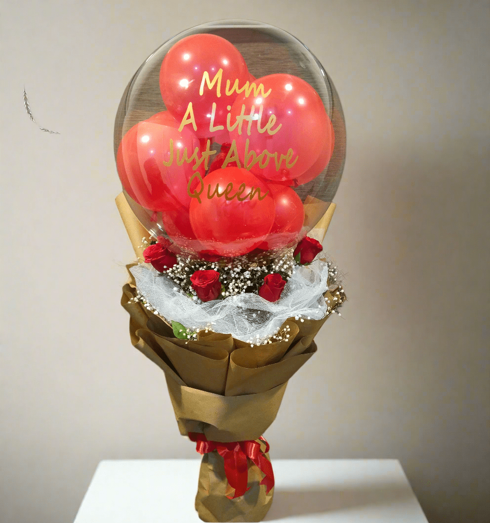 A balloon bouquet arrangement with a transparent balloon, red roses, and baby's breath, wrapped with premium wrapping sheets.