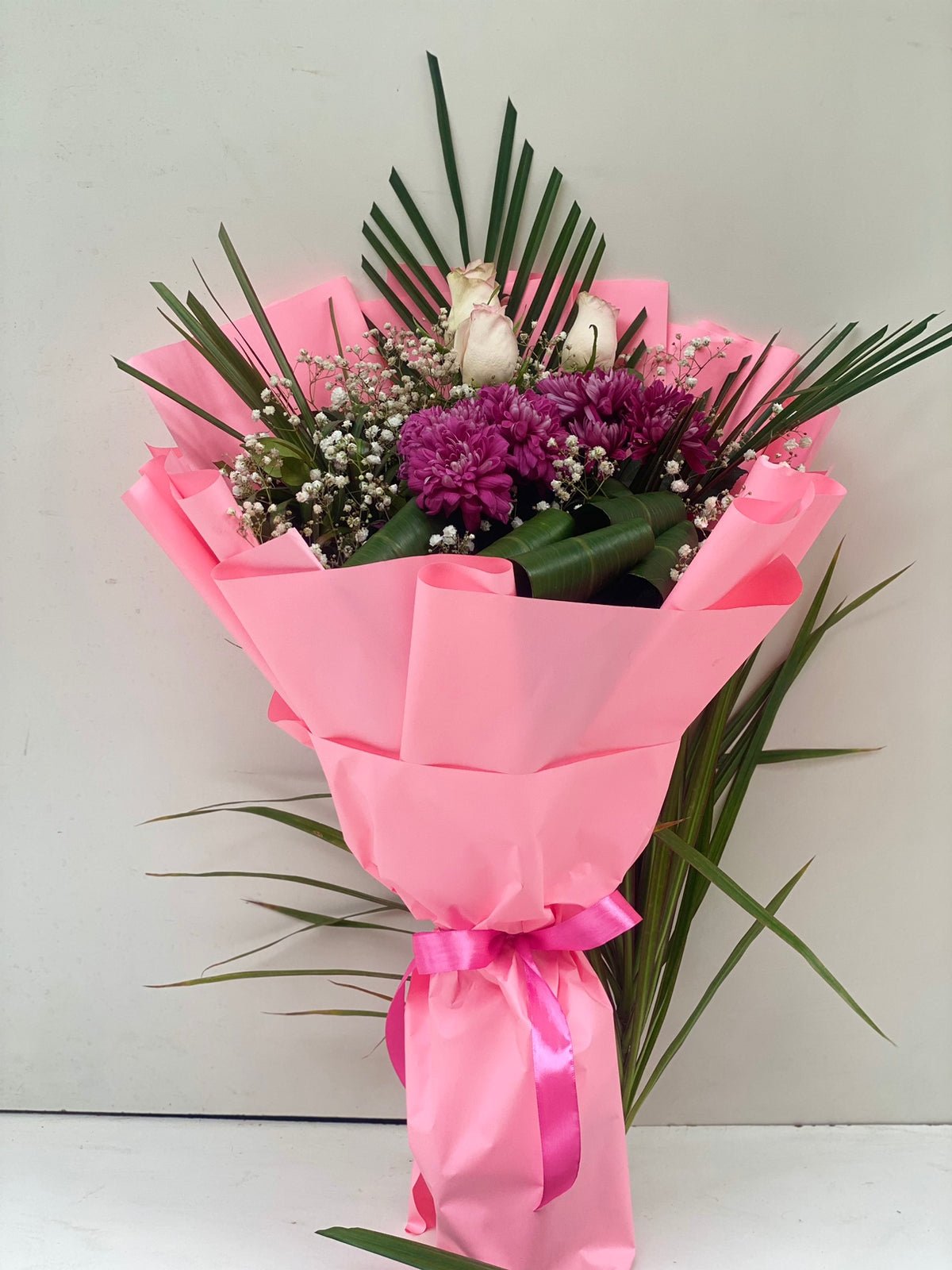 A bouquet of flowers including roses, chrysanthemums, and baby's breath, wrapped in pink paper with a ribbon.