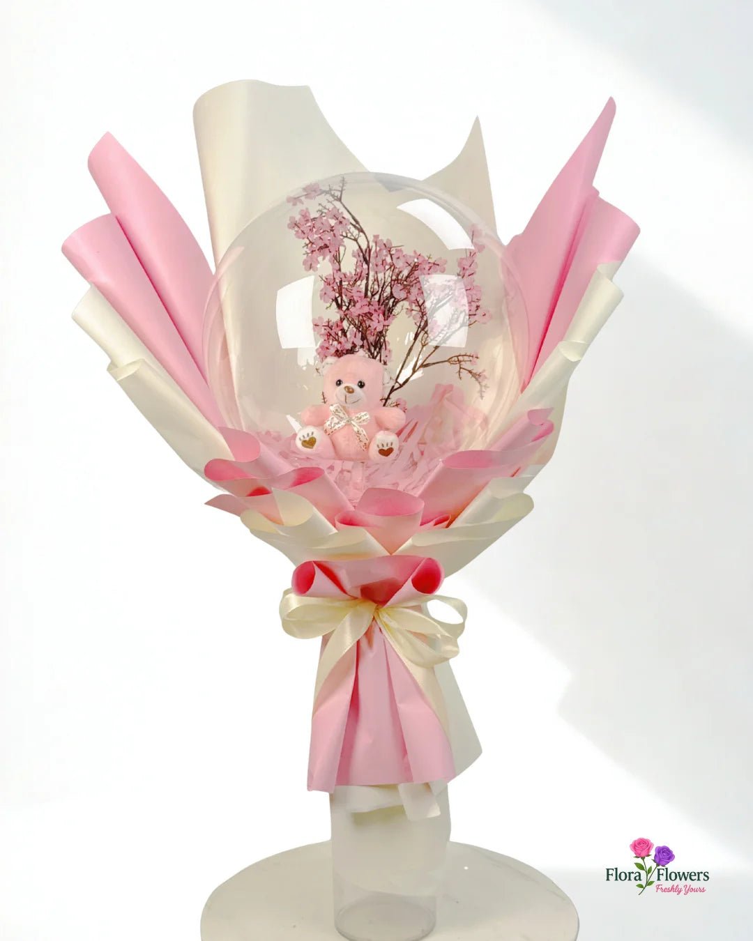 Bouquet with pink and white ribbons and a small teddy bear on a white background, featuring the brand 'Flora & Flowers'.. Send flowers to lahore. send flowers to Pakistan