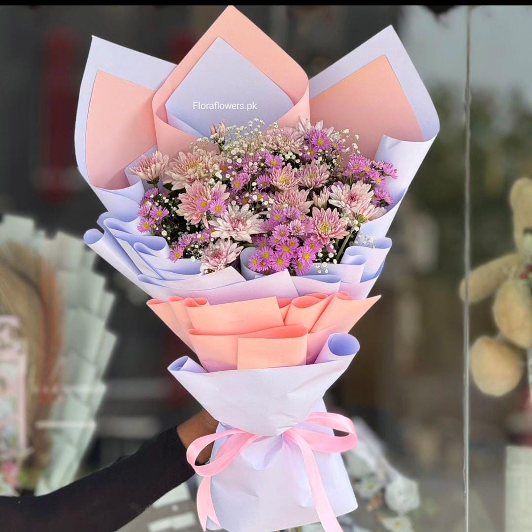 A bouquet of flowers consisting of chrysanthemums and Baby's Breath, wrapped in pink and purple paper with a ribbon.