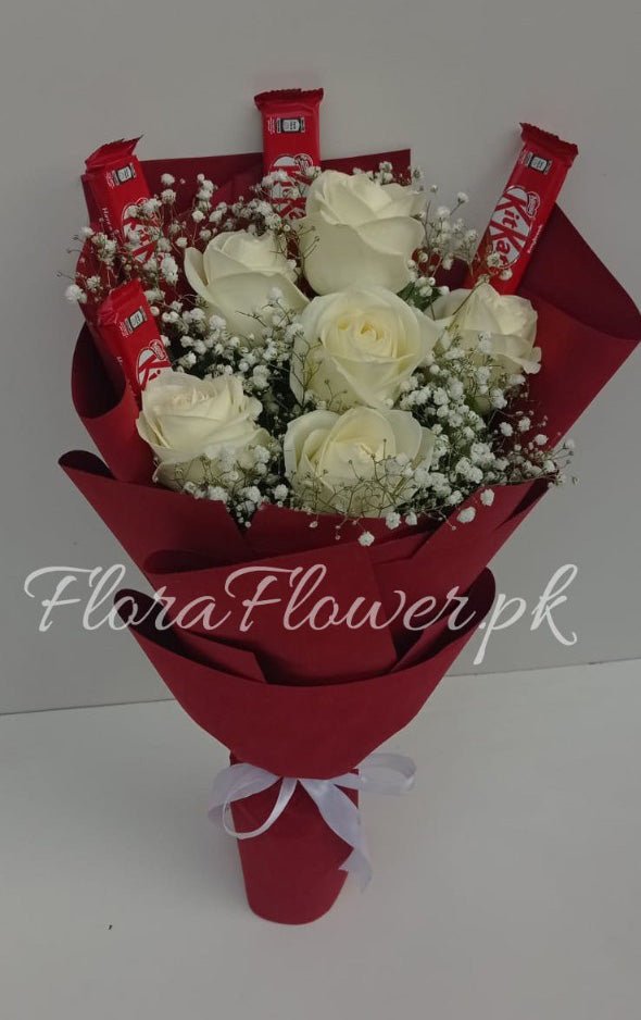 A bouquet of white roses with baby's breath, wrapped with a red and white themed wrapping paper, accompanied by KitKat chocolate bars.