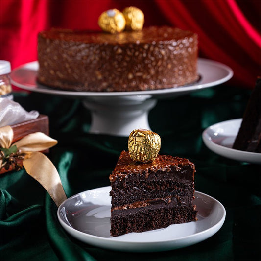 Chocolate cake with a gold candy on top, served on a white plate with a red curtain background.