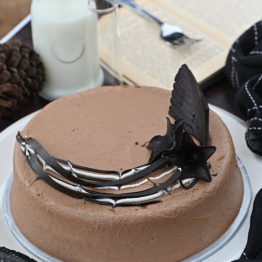 Chocolate cake with decorative elements on a white plate, surrounded by a glass of milk and a book.