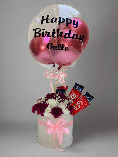A gift arrangement featuring a round white box with pink ribbon, containing three stems of white chrysanthemum, three stems of purple chrysanthemum, and a 'Happy Birthday' customized balloon, alongside three KitKat and three Dairy Milk chocolate bars. Send flowers to islamabad. send flowers to pakistan