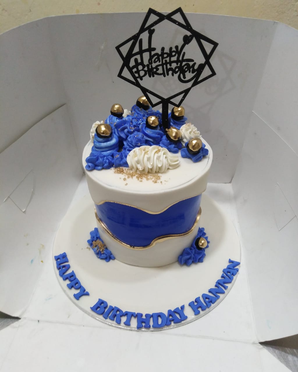 Birthday cake with blue and white design, gold accents, and 'Happy Birthday Hannan' text.