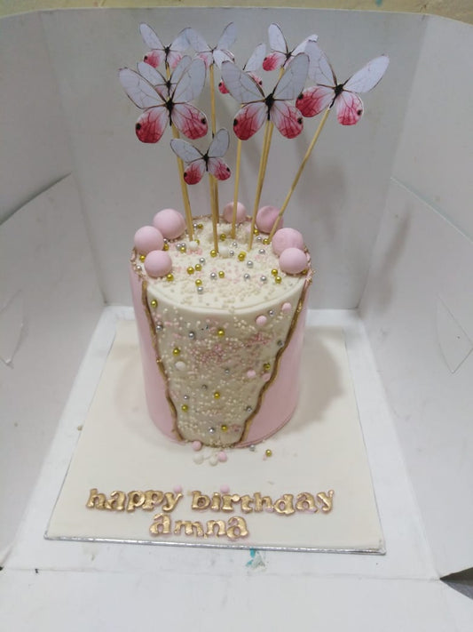 Decorative cake with butterfly toppers on a white stand, featuring the text 'happy birthday amna'.