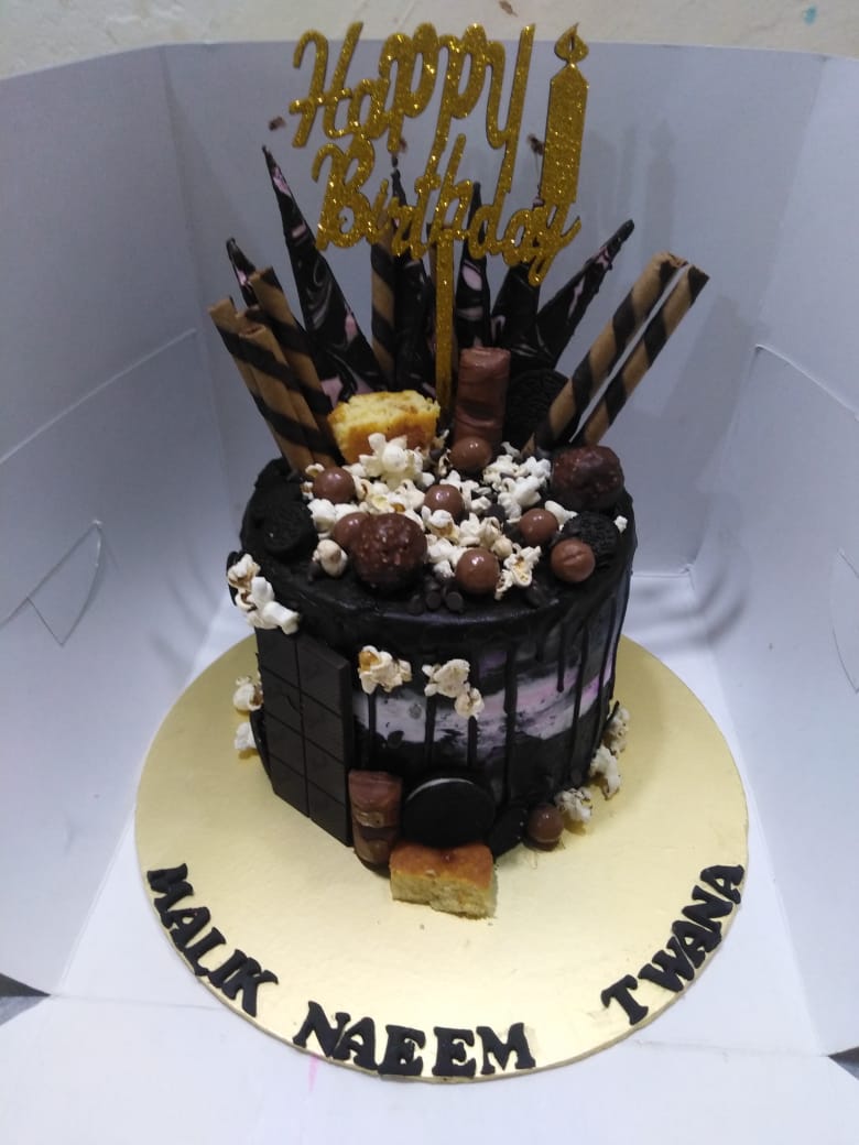 A decorated chocolate monster cake with various toppings and a 'Happy Birthday' topper in gold color.