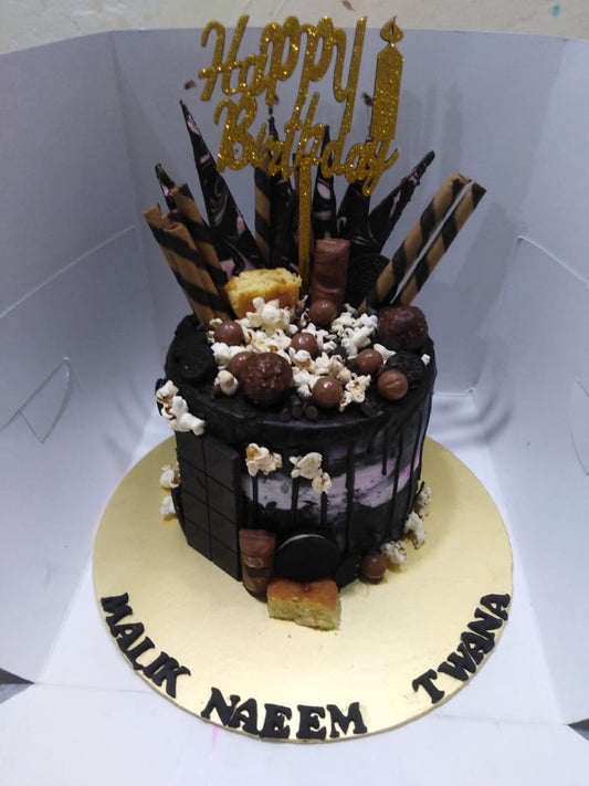 A decorated chocolate monster cake with various toppings and a 'Happy Birthday' topper in gold color.