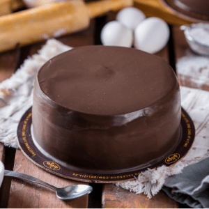 Chocolate cake on a wooden board with a spoon and marshmallows in the background