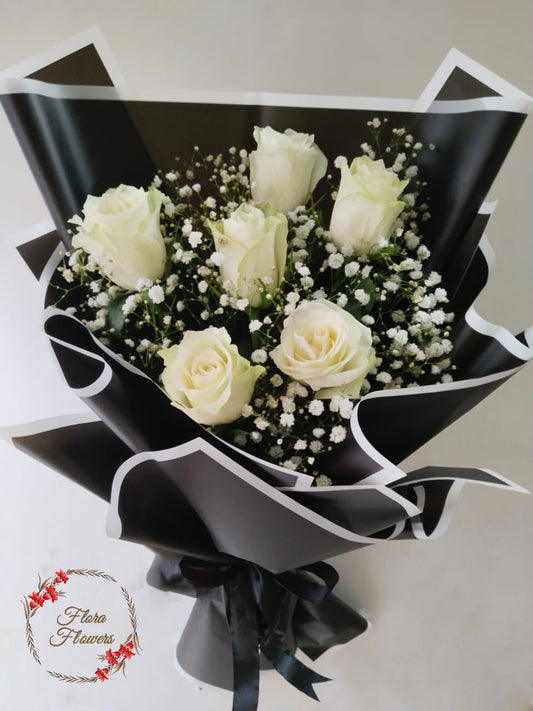 A bouquet of white roses with baby's breath, wrapped in black and white premium wrapping paper with ribbon.
