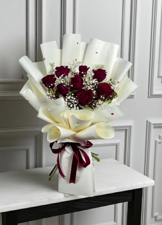 Bouquet of red roses and white calla lilies on a marble table with a white wall background
