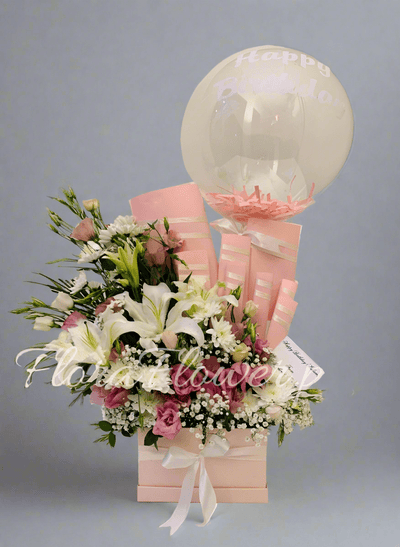 A gift basket containing an assortment of chocolates and a balloon, adorned with an artificial floral arrangement. Send flowers to islamabad. send flowers to pakistan