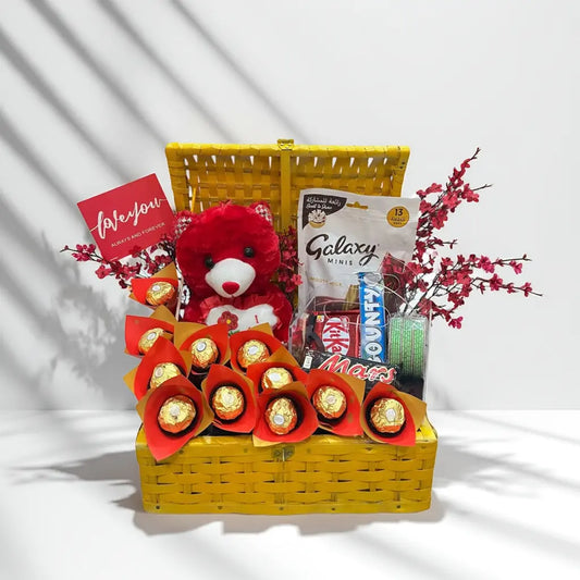 Gift basket with teddy bear, chocolates, and snacks on a white background