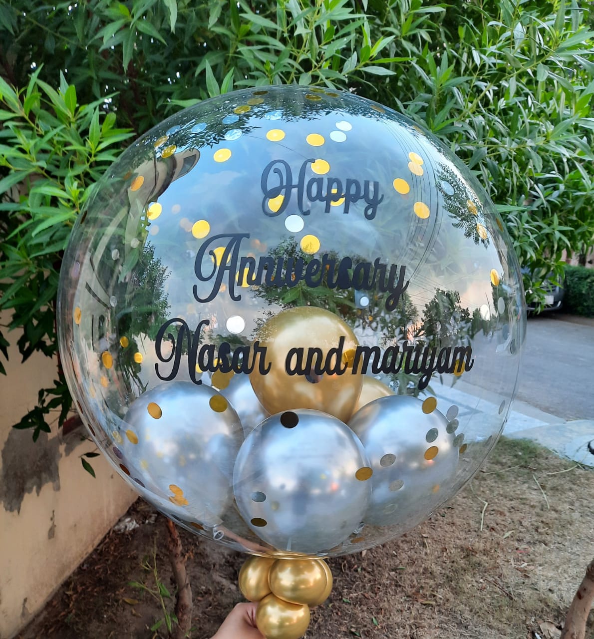 Clear balloon with gold and silver balloons inside, featuring 'Happy Anniversary Nasir and Mariam' text.