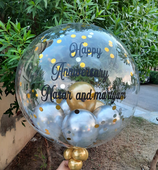 Clear balloon with gold and silver balloons inside, featuring 'Happy Anniversary Nasir and Mariam' text.