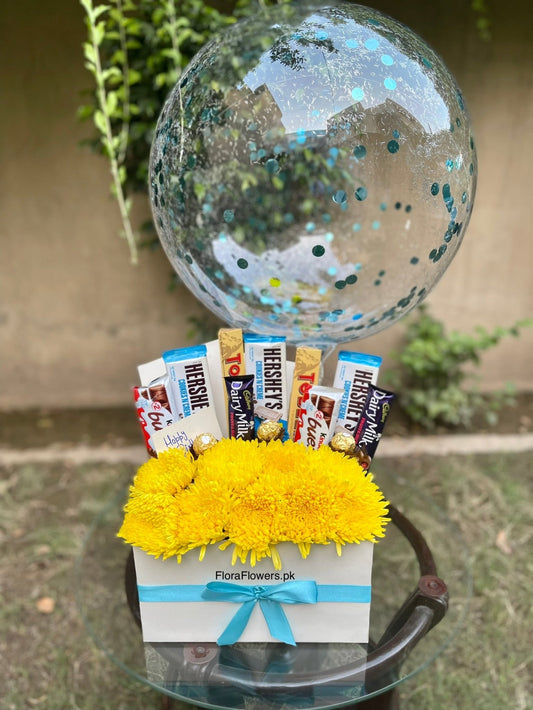 Gift basket with candy bars and yellow flowers on a small table outdoors.
