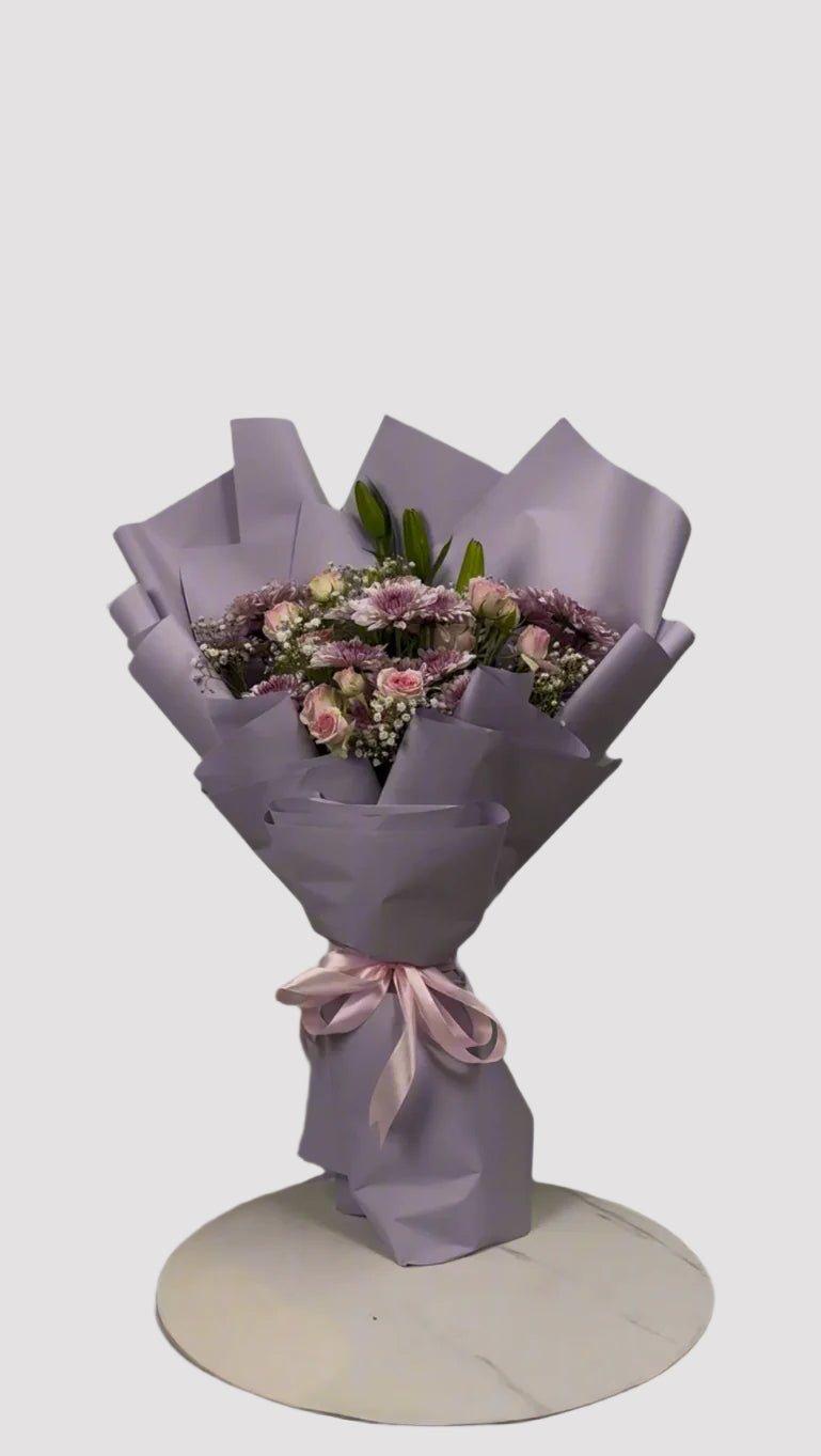 A bouquet of flowers including chrysanthemums, spray roses, a lily, and baby's breath, wrapped in purple paper with a pink ribbon . Send flowers to islamabad. send flowers to pakistan