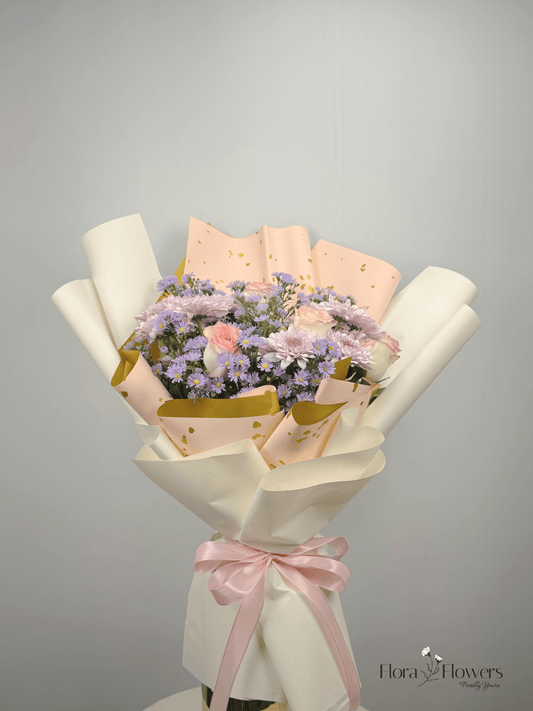 A bouquet of flowers including roses, chrysanthemums, and baby's breath, wrapped in white and pink paper with a ribbon.