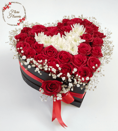 A heart-shaped floral arrangement basket with red roses and white flowers, adorned with a red ribbon.
