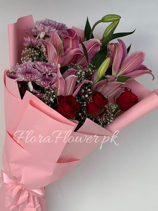 A bouquet of imported roses, chrysanthemums, lilies, and baby's breath wrapped in pink sheets with the brand 'FloraFlower.pk' visible.