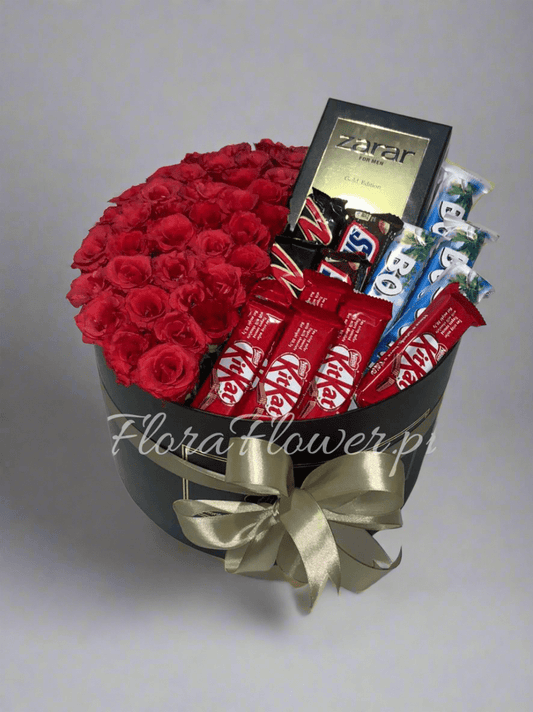 A round arrangement of red roses with chocolate bars and a bottle of perfume, tied with a gold ribbon.