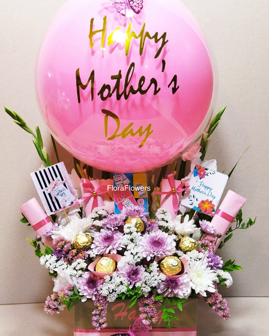 A Mother's Day gift arrangement featuring a pink balloon, flowers in shades of pink and white, and an assortment of chocolates.