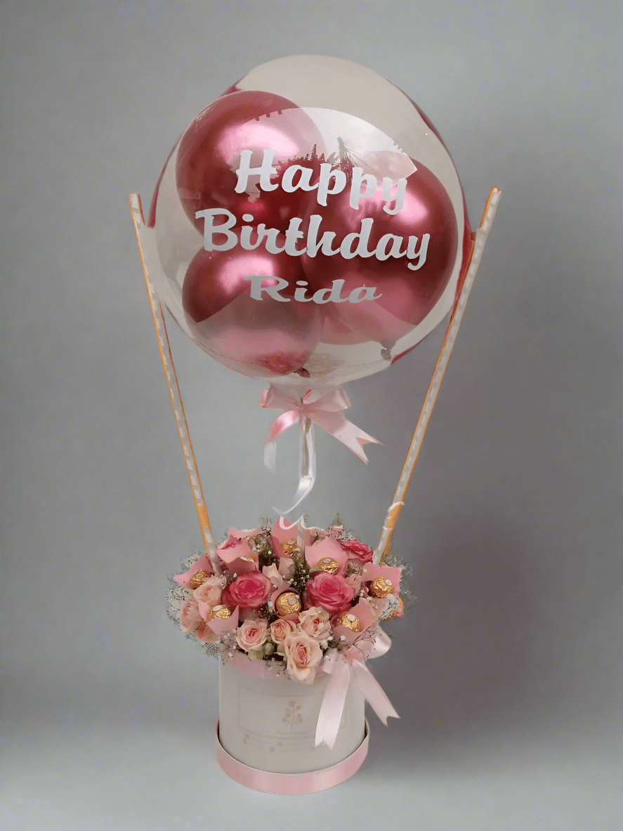 A pink and white floral arrangement with a 'Happy Birthday' balloon, roses, and a box of chocolates. Send flowers to islamabad. send flowers to pakistan