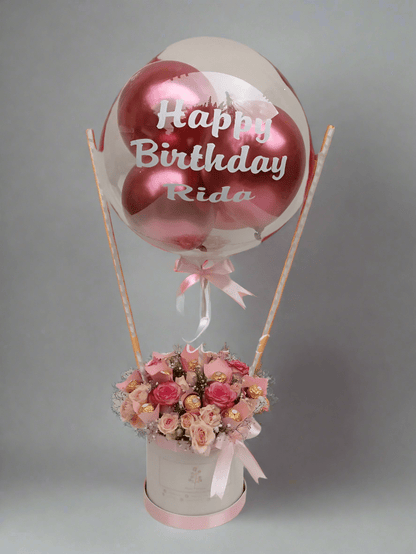 A pink and white floral arrangement with a 'Happy Birthday' balloon, roses, and a box of chocolates. Send flowers to islamabad. send flowers to pakistan
